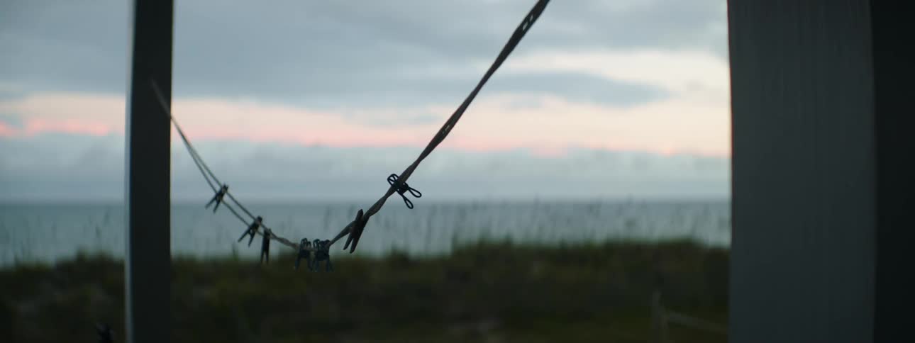 Empty clothesline sways in breeze against pink tinted horizon