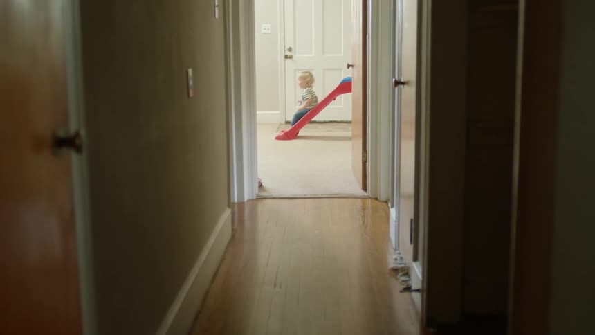 A blonde toddling playing on a slide indoors at home