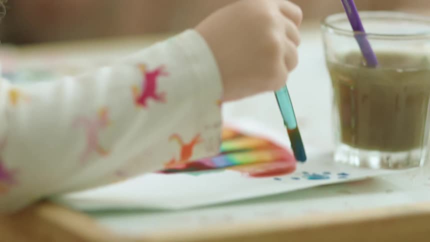 A child paints blue dots onto paper with a brush and water color paints