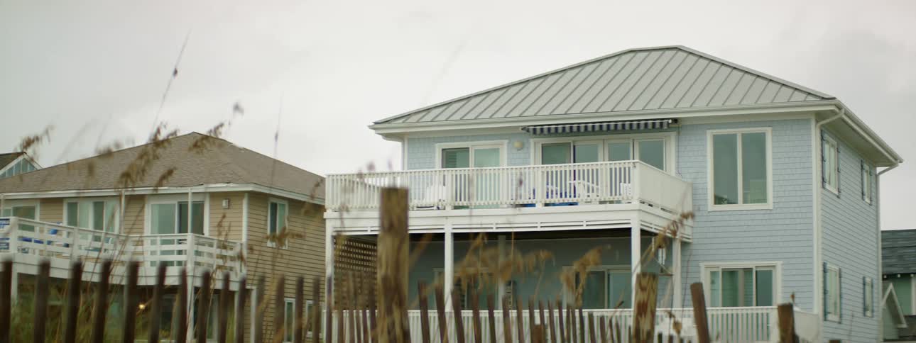 Houses with a fence and plants in the foreground and the sky and clouds in the background
