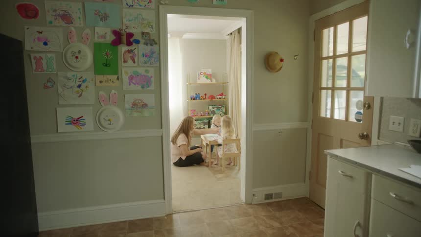 A woman sits on the ground next to her daughters in a playroom at home