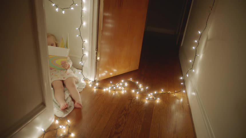Blonde girl lying down in room near dark hallway lit by string of small white lights