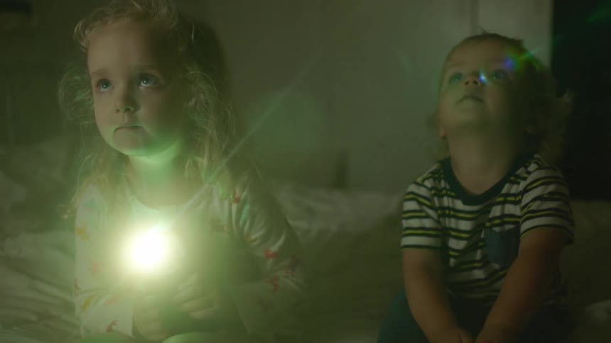 A little boy sits looking upwards as a little girl next to him shines a flashlight