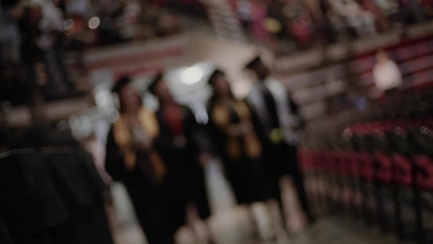 Blurry view of graduates smiling at a crowd as they walk by