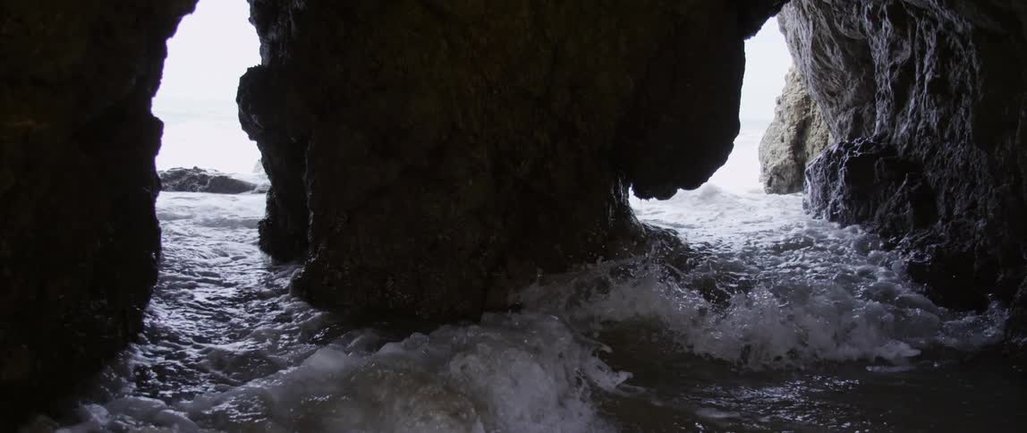 Water rushes past a large rock formation in the ocean during the day
