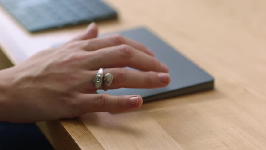 A person sliding fingers over a trackpad next to a keybard