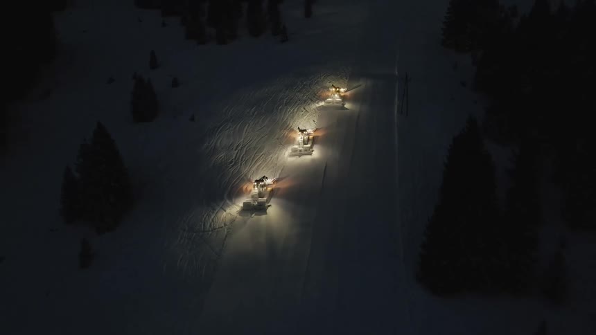 An aerial view of three snow plows clearing snow at night