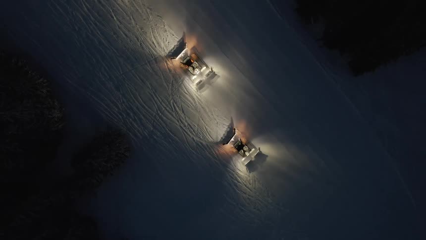 Vehicles plowing snow surrounded by trees