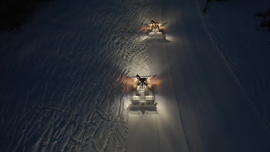 Lights on two slow moving snowplows lighten up road passing through forest