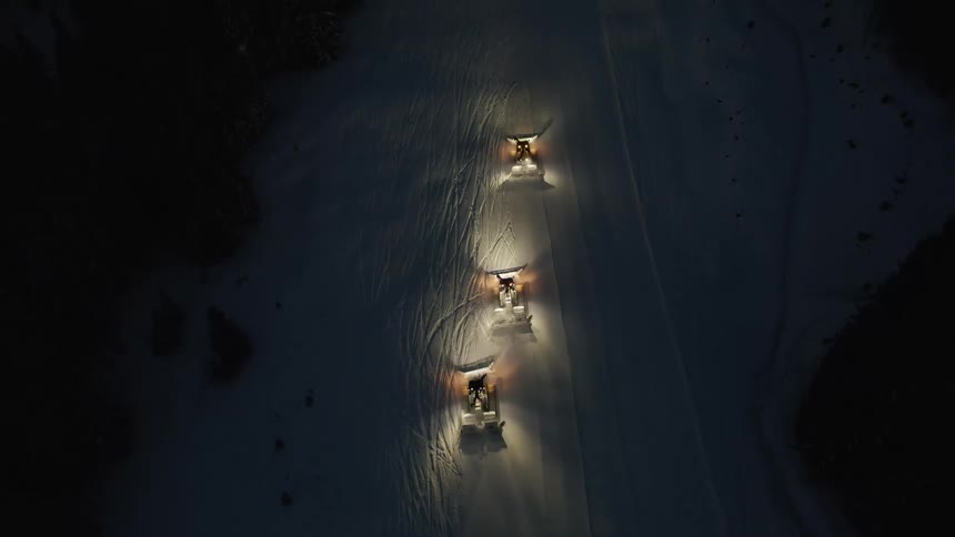 Aerial birds eye view of snow cats grooming snow at night