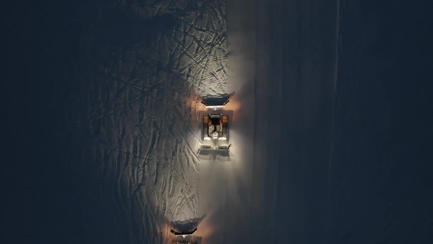 Birds eye view of snow cats grooming a ski run at night