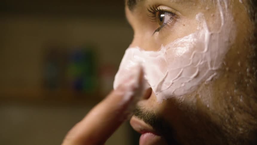 A man applies a thick layer of a white face mask to his nose and cheeks