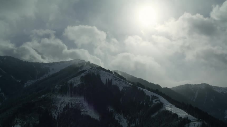 A mountain range is covered in snow and dense trees under a cloudy sky