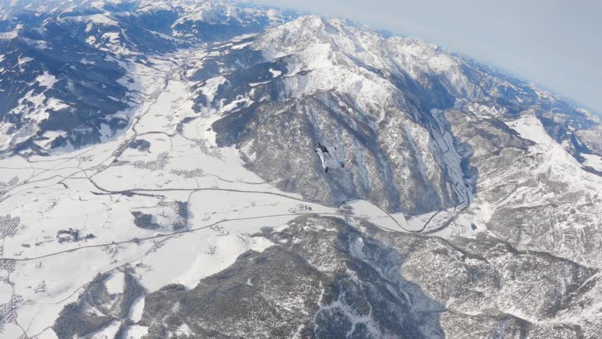 Skydiver wearing a wing suit is gliding over snow covered mountains