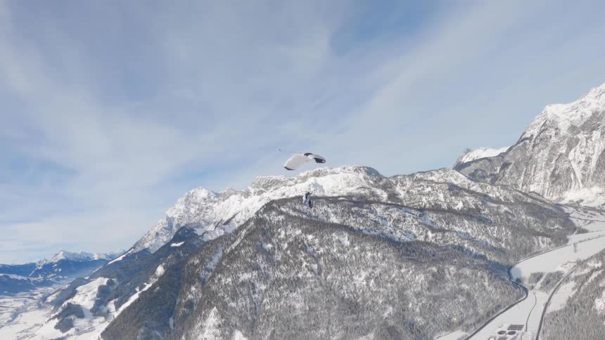 A person paragliding with a snow covered mountain range the sky and clouds in the background
