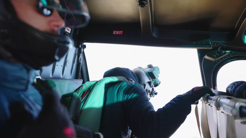 Two men with coats and helmets and gloves in an aircraft one with a camera on his helmet