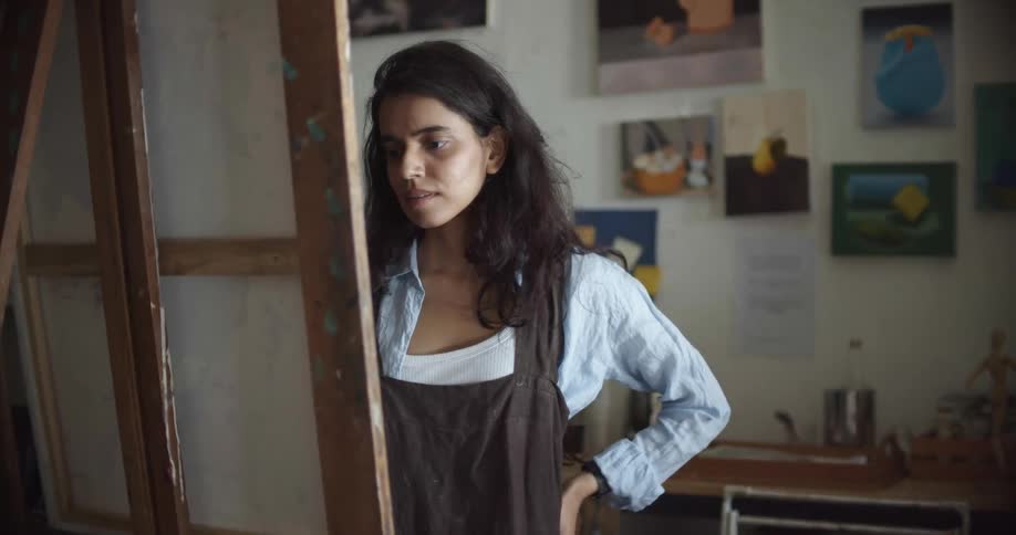 A young woman painting steps back and looks at her work