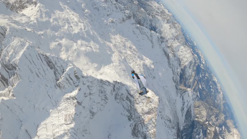 Skydiver wearing a wing suit is floating and gliding over a snow covered mountain range