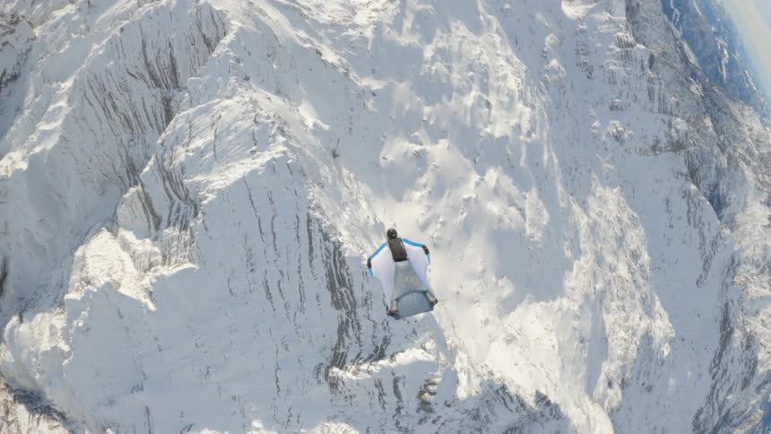 An aerial view of a person gliding over snowy mountains in the wilderness