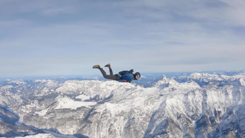 A man turning in the air as he sky dives above the mountains