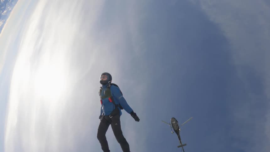 A person with a helmet jumping off of a helicopter and skydiving with the sky and clouds in the background