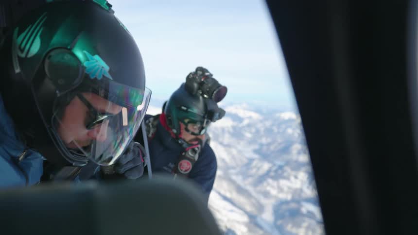 Two men staring down at a snowy mountain range from a helicopter during the day