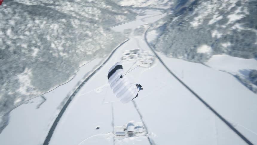 A skydiver with a white parachute floats over a snow covered landscape