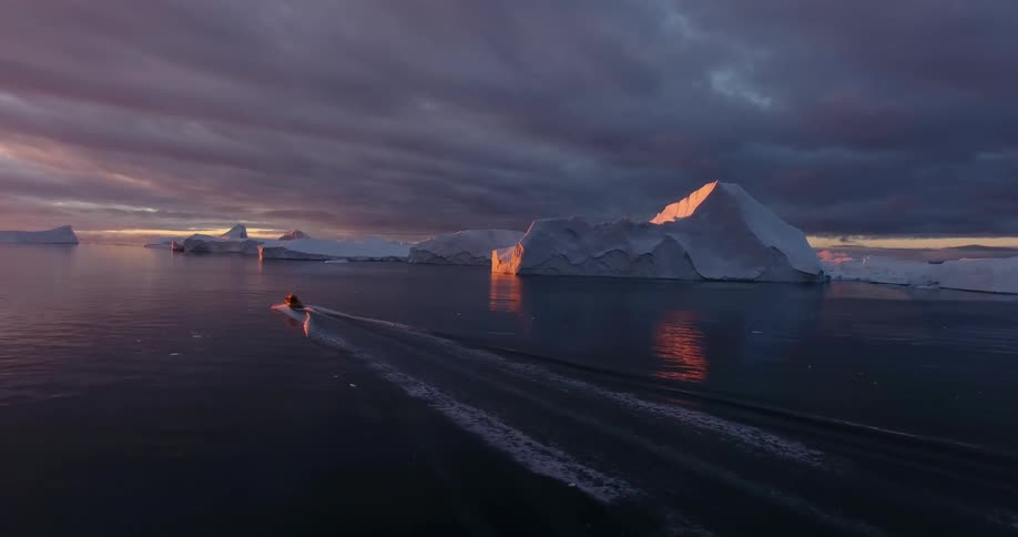 A boat travels past icebergs in the arctic ocean in the evening