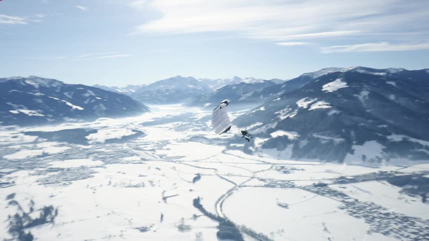 Person wearing a parachute is gliding over a snow covered mountain canyon