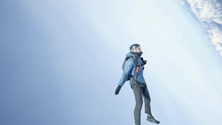 Skydiver wearing a parachute pack and black helmet is floating over snow covered mountains
