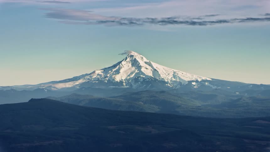 Mount Hood rises dramatically in winter in this aerial as snow blows off the summit under a clear blue sky