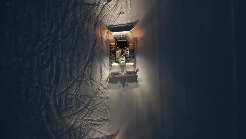 Aerial birds eye view of snow cats grooming snow at night