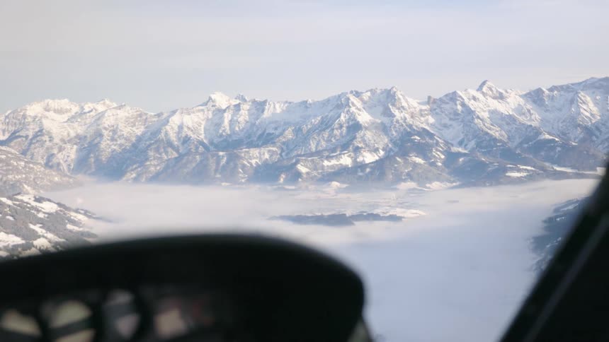 A person in the cockpit of an aircraft with a mountain range the sky and clouds in the background