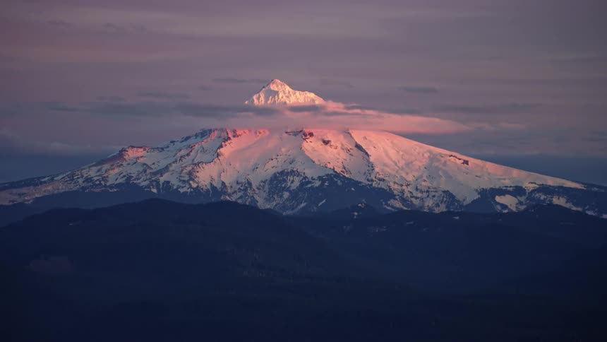 Slow zoom out reveal of Mount Hood in winter at sunset with wispy clouds clinging to the summit under perfect blue hour light