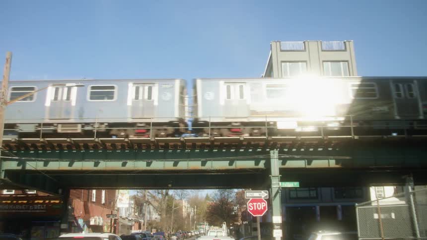 A train travels along an overpass over an intersection in a city on a sunny day
