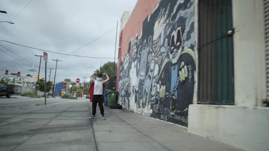 A young boy flexing his arms while pretending to be a superhero on a city sidewalk