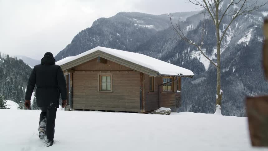 A man walking towards a cabin in the snow on a mountain