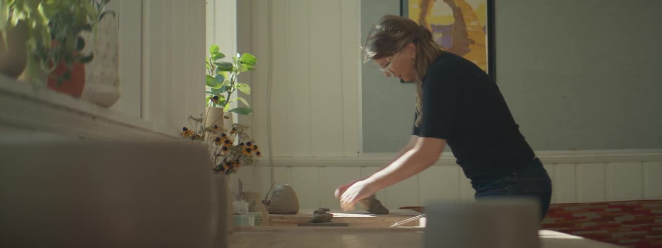 A woman in a room with glasses rolling clay on a table