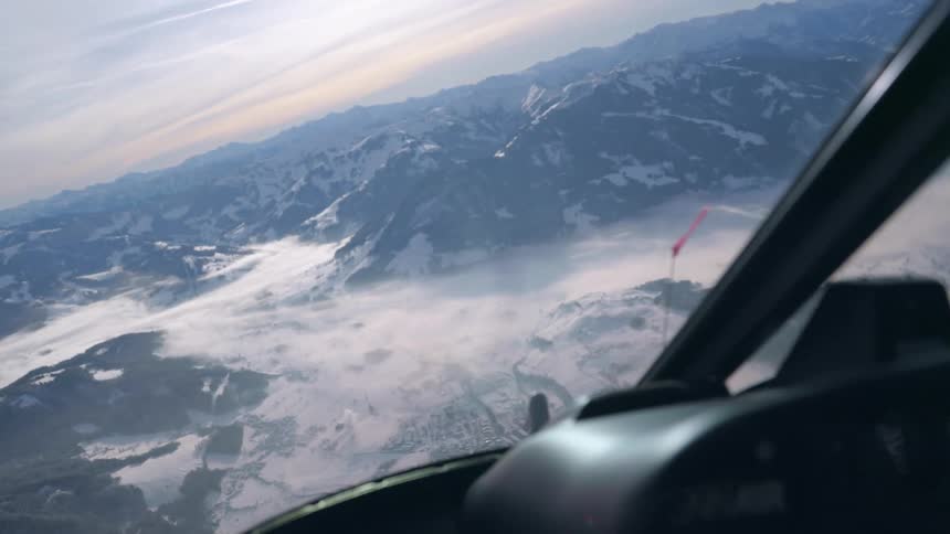 A snowy mountain range view from inside of a helicopter high in the sky during the day