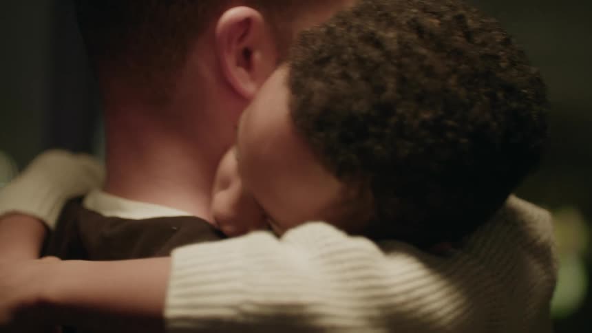 A man holds a boy in his arms as he gazes out the window at night