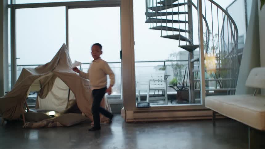 A boy attempts to keep his balance as he runs around a marble floor in his socks before he stops and throws a paper airplane towards the camera