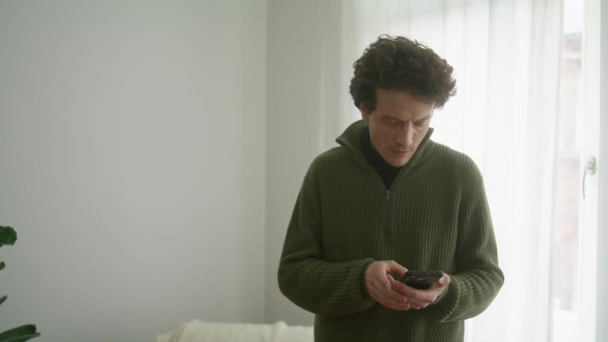 Young man waiting impatiently for a call on his smartphone in a room at home