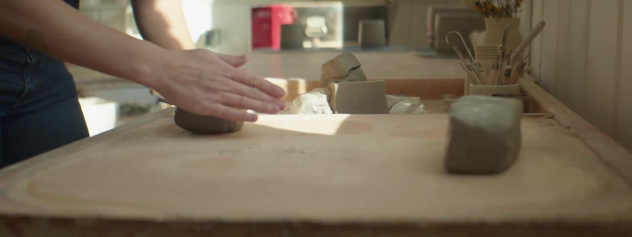 A woman in a room with glasses shaping clay on a table