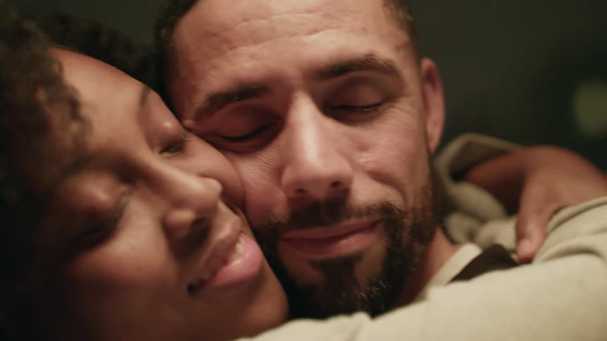 Young couple lovingly hugging cheek to cheek in the living room at home