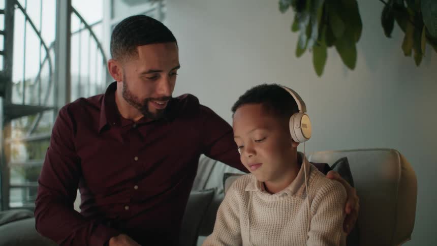 A father kissing his son on the head while he listens to music with headphones