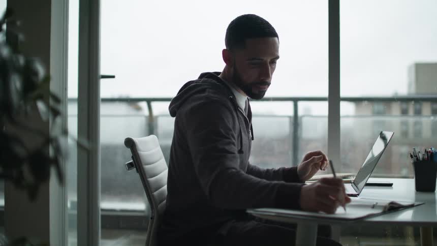 A man is writing and using his keyboard at the desk