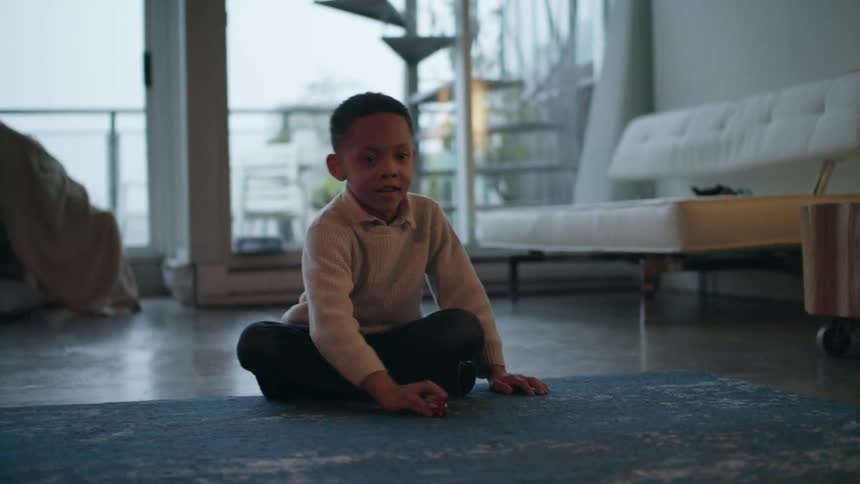 A boy in a room sitting on the floor and playing with a toy car with a couch in the background