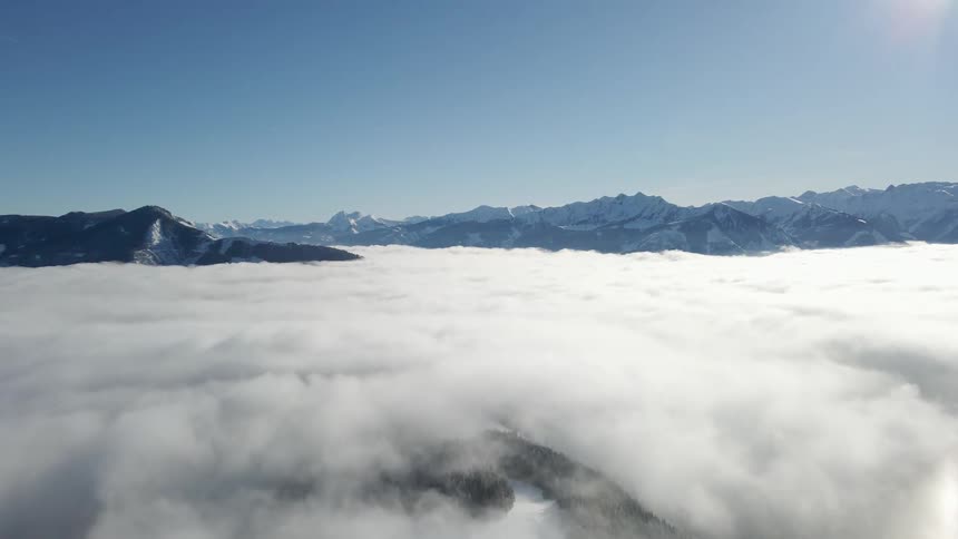 Snowy mountain ridges poke through thick mist under a clear blue daytime sky
