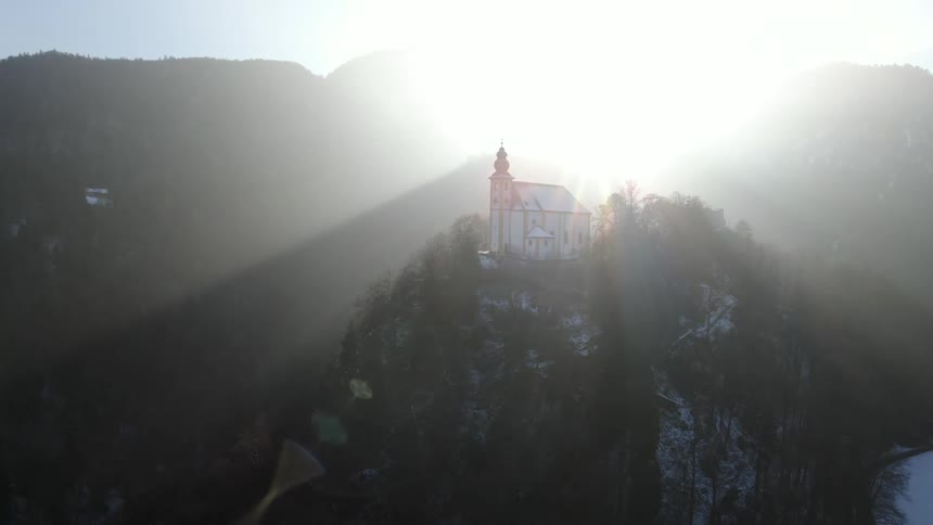 A small church sits on top of a tree covered mountain peak