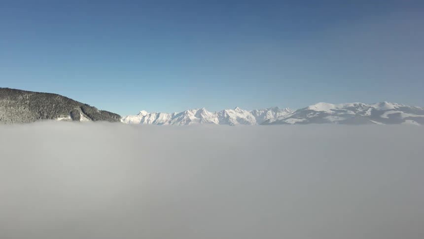 Cloud rising in front of snow covered mountains high in a blue sky